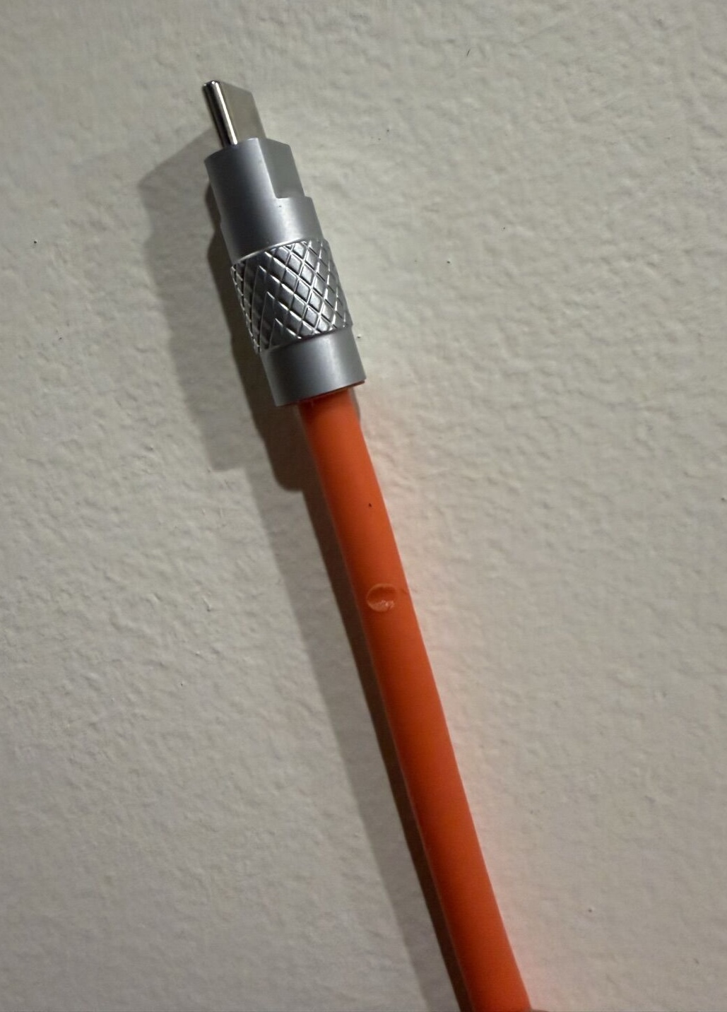 The orange Thzzhnno cable with its knurled metal USB-C connector, showing a melted spot from my soldering iron